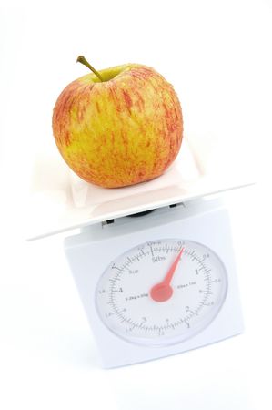 A red apple on top of a set of kitchen scales isolated against a white backgroundの写真素材
