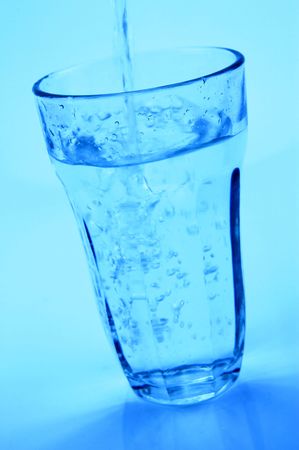 Water pouring into a glass isolated against a blue backgroundの写真素材