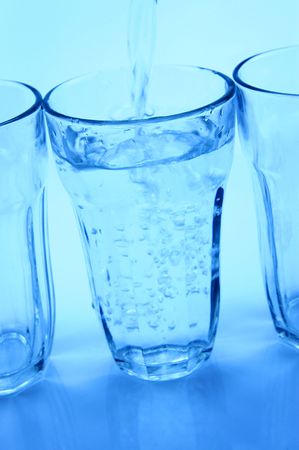 Water pouring into a glass isolated against a blue backgroundの写真素材