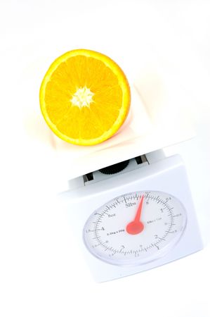 A sliced orange on top of a set of kitchen scales isolated against a white backgroundの写真素材