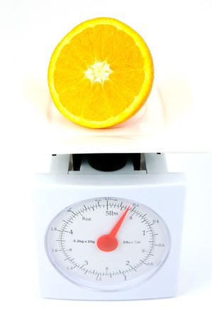 A sliced orange on top of a set of kitchen scales isolated against a white backgroundの写真素材