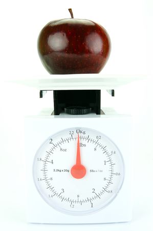A red apple on top of a set of kitchen scales isolated against a white backgroundの写真素材