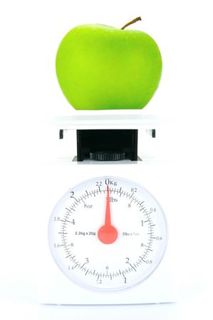 A green apple on top of a set of kitchen scales isolated against a white backgroundの写真素材