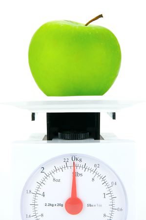 A green apple on top of a set of kitchen scales isolated against a white backgroundの写真素材