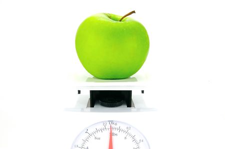 A green apple on top of a set of kitchen scales isolated against a white backgroundの写真素材