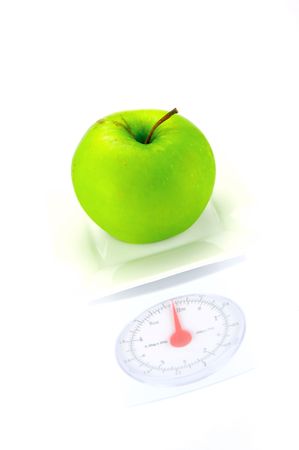 A green apple on top of a set of kitchen scales isolated against a white backgroundの写真素材