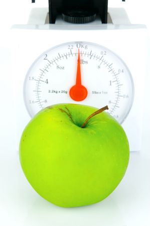 A green apple on top of a set of kitchen scales isolated against a white backgroundの写真素材