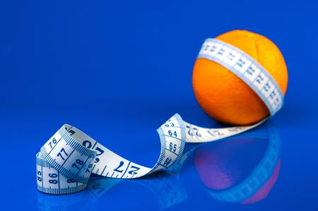Conceptual health and diet image of an orange and a measuring tape isolated against a blue backgroundの写真素材