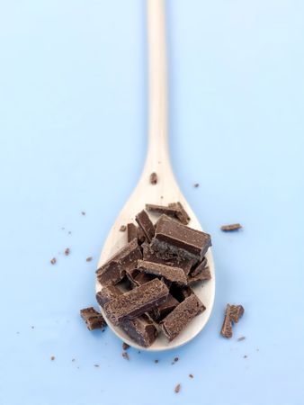 Cooking chocolate chopped on a wooden spoon isolated against a blue backgroundの写真素材