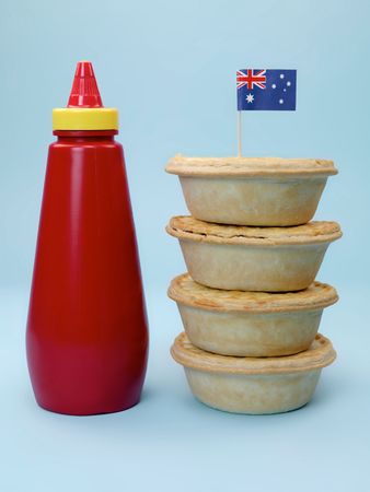 A stack of  Australian meat pies isolated against a blue background with a bottle of tomato sauceの写真素材
