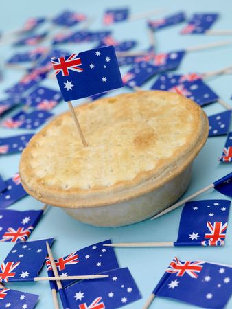 An Australian meat pie isolated against a blue background with Australian flagsの写真素材