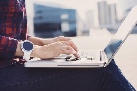 Young woman wearing smart watch using laptop computer. Female hands working on laptop outdoorの写真素材