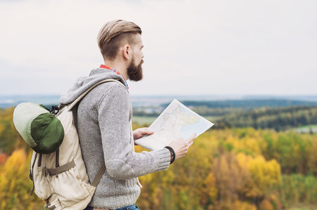 Young man traveler standing on top of the hill and looking to the map. Travel and active lifestyle conceptの写真素材