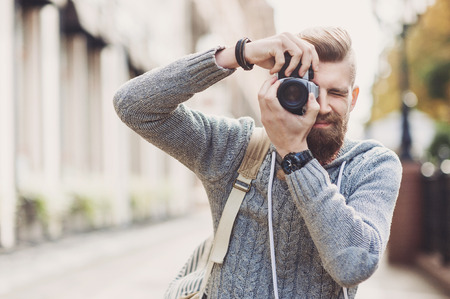 Young cheerful man photographer takes images with cameraの写真素材
