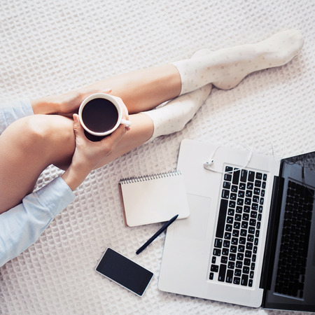 Young woman drinking coffee and using laptop at homeの写真素材
