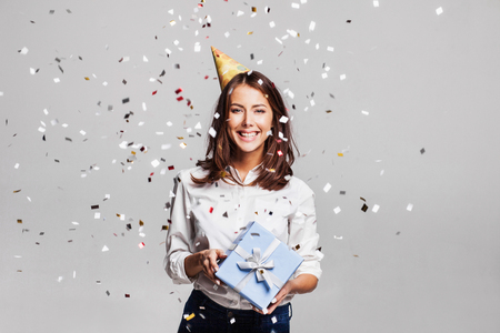 Beautiful happy woman with gift box at celebration party with confetti falling everywhere on her. Birthday or New Year eve celebrating conceptの写真素材