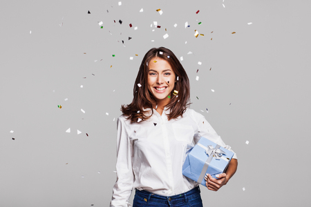 Beautiful happy woman with gift box at celebration party with confetti falling everywhere on her. Birthday or New Year eve celebrating conceptの写真素材