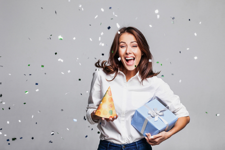 Beautiful happy woman with gift box at celebration party with confetti falling everywhere on her. Birthday or New Year eve celebrating conceptの写真素材