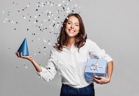 Beautiful happy woman with gift box at celebration party with confetti falling everywhere on her. Birthday or New Year eve celebrating conceptの写真素材