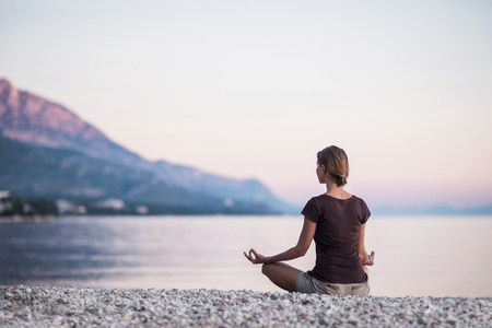 Young woman practicing yoga near the sea. Harmony and meditation concept. Healthy lifestyleの写真素材