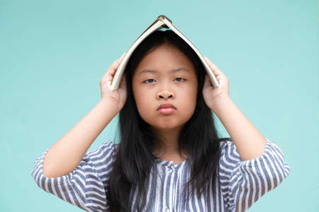 Asian little girl standing and holding a book over her head on a green background. Back to school, Study from home.の写真素材