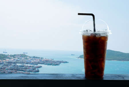 Ice black coffee or iced americano in plastic cuo with straw at outdoor coffee shop with freshly day, blue sky and sea port backgroundの写真素材
