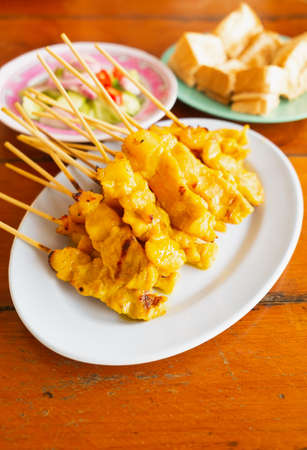 Closed up street food it's grill pork satay or grilled pork on white dish served with bean sauce and pickle cucumbers and onions in vinegar.の写真素材
