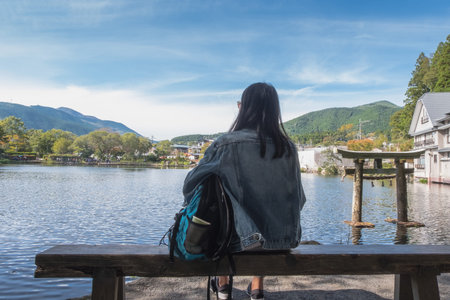 Woman sitting on the chair at Lake Kinrin and Japanese gate (Torii) with Mount Yufu and blue sky...