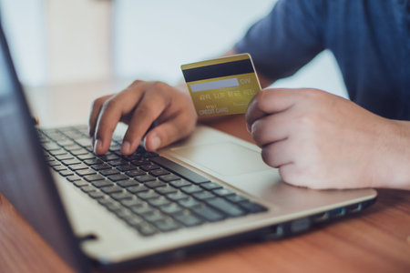 man holding credit card while using laptop for online shopping with selective focus on the credit...