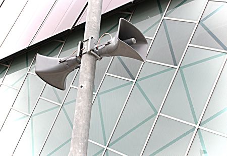 speakers hung up on a post againt a decorative buildingの写真素材