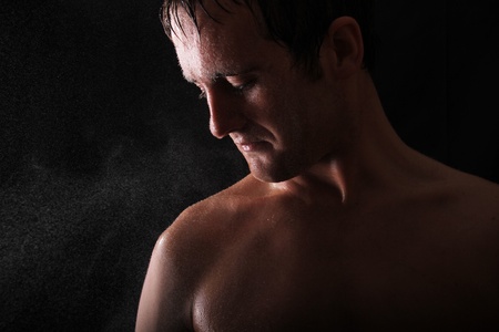 male model standing against a black background with light shining in his face. water is also sprayed in the face of the modelの写真素材