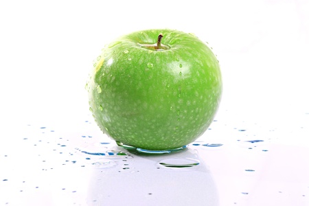 a bright green apple on white with water droplets on itの写真素材