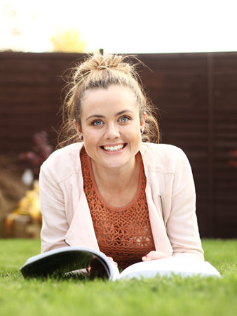 a beautiful young girl relaxes outside reading a book whilst lay down on grass.の写真素材