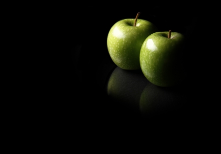 two apples lay on a reflective surface lit by one light with lots of copy space.の写真素材