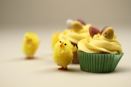 easter cakes with tiny easter eggs on top of the icing, with little yellow chicks around the cakes の写真素材