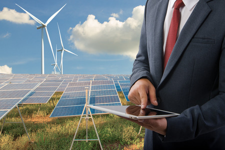 Businessman holding a tablet at Solar panels with wind turbines  blue sky with clouds background and (solar cell)  create the clean electric power Business Concept.の写真素材