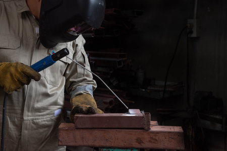 A welder is welding steel in an industrial factory. The welder wears protective clothing to work in...