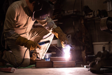 A welder is welding steel in an industrial factory. The welder wears protective clothing to work in...