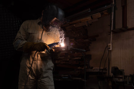 A welder is welding steel in an industrial factory. The welder wears protective clothing to work in...