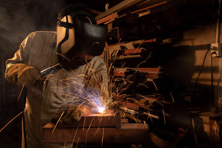 A welder is welding steel in an industrial factory. The welder wears protective clothing to work in the workplace.の写真素材