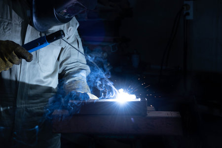 A welder is welding steel in an industrial factory. The welder wears protective clothing to work in...