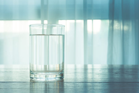 Glass of water on wooden table and light blurred background