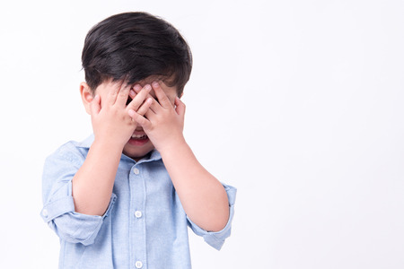 Kid covering his eyes over white background wearing blue shirtの写真素材