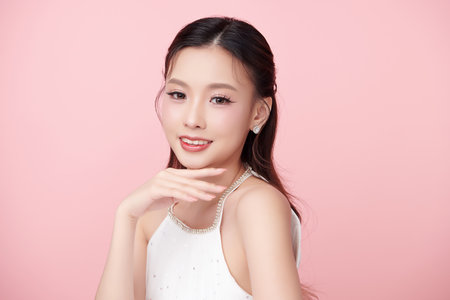 A beautiful young Asian woman with clean, fresh skin against a pink background. Skincare, facial treatment, cosmetology, beauty, and spa. An elegant portrait of an Asian woman.の写真素材