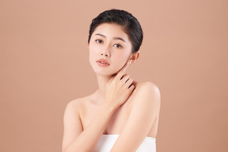 A beautiful young Asian woman with clean, fresh skin against a beige background. Skincare, facial treatment, cosmetology, beauty, and spa. An elegant portrait of an Asian woman.の写真素材