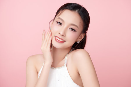 A beautiful young Asian woman with clean, fresh skin against a pink background. Skincare, facial treatment, cosmetology, beauty, and spa. An elegant portrait of an Asian woman.の写真素材