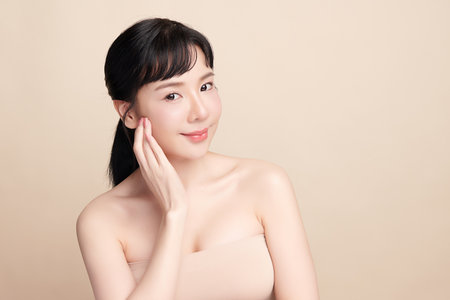 A beautiful young Asian woman with clean, fresh skin against a beige background. Skincare, facial treatment, cosmetology, beauty, and spa. An elegant portrait of an Asian woman.の写真素材