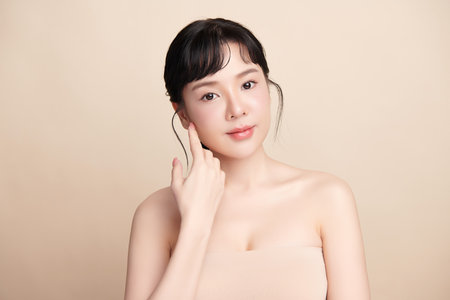 A beautiful young Asian woman with clean, fresh skin against a beige background. Skincare, facial treatment, cosmetology, beauty, and spa. An elegant portrait of an Asian woman.の写真素材