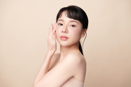 A beautiful young Asian woman with clean, fresh skin against a beige background. Skincare, facial treatment, cosmetology, beauty, and spa. An elegant portrait of an Asian woman.の写真素材