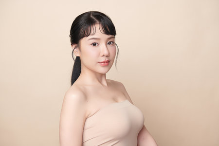 A beautiful young Asian woman with clean, fresh skin against a beige background. Skincare, facial treatment, cosmetology, beauty, and spa. An elegant portrait of an Asian woman.の写真素材